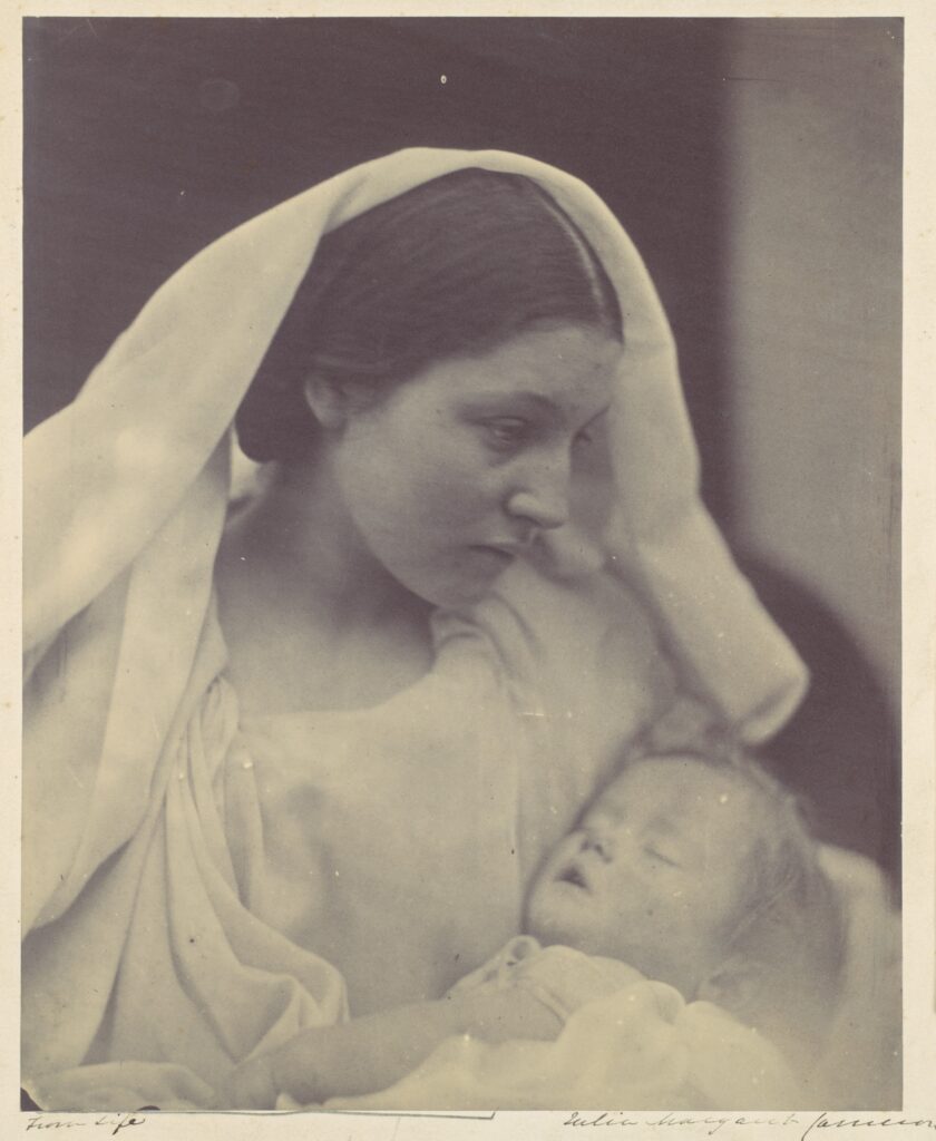 Black-and-white portrait of a mother in a head covering gazing down at her child.