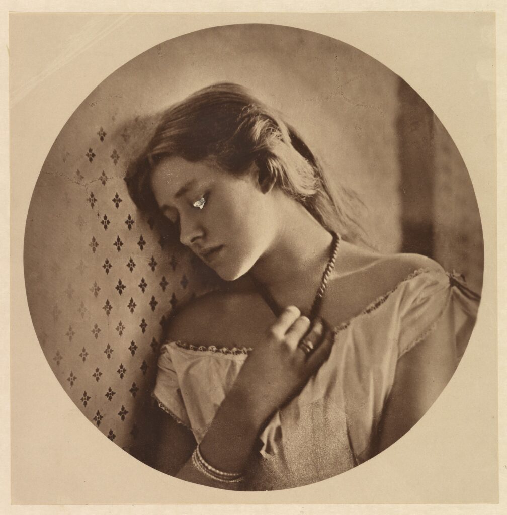 Sepia-toned portrait of a young woman resting her head against a wall, looking down thoughtfully.
